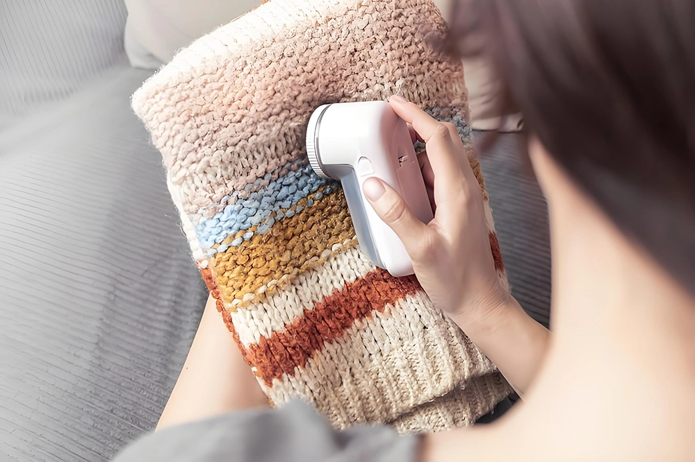 Close-up of a person using a fabric shaver to remove lint — demonstrating merino wool care for keeping garments fresh and smooth.